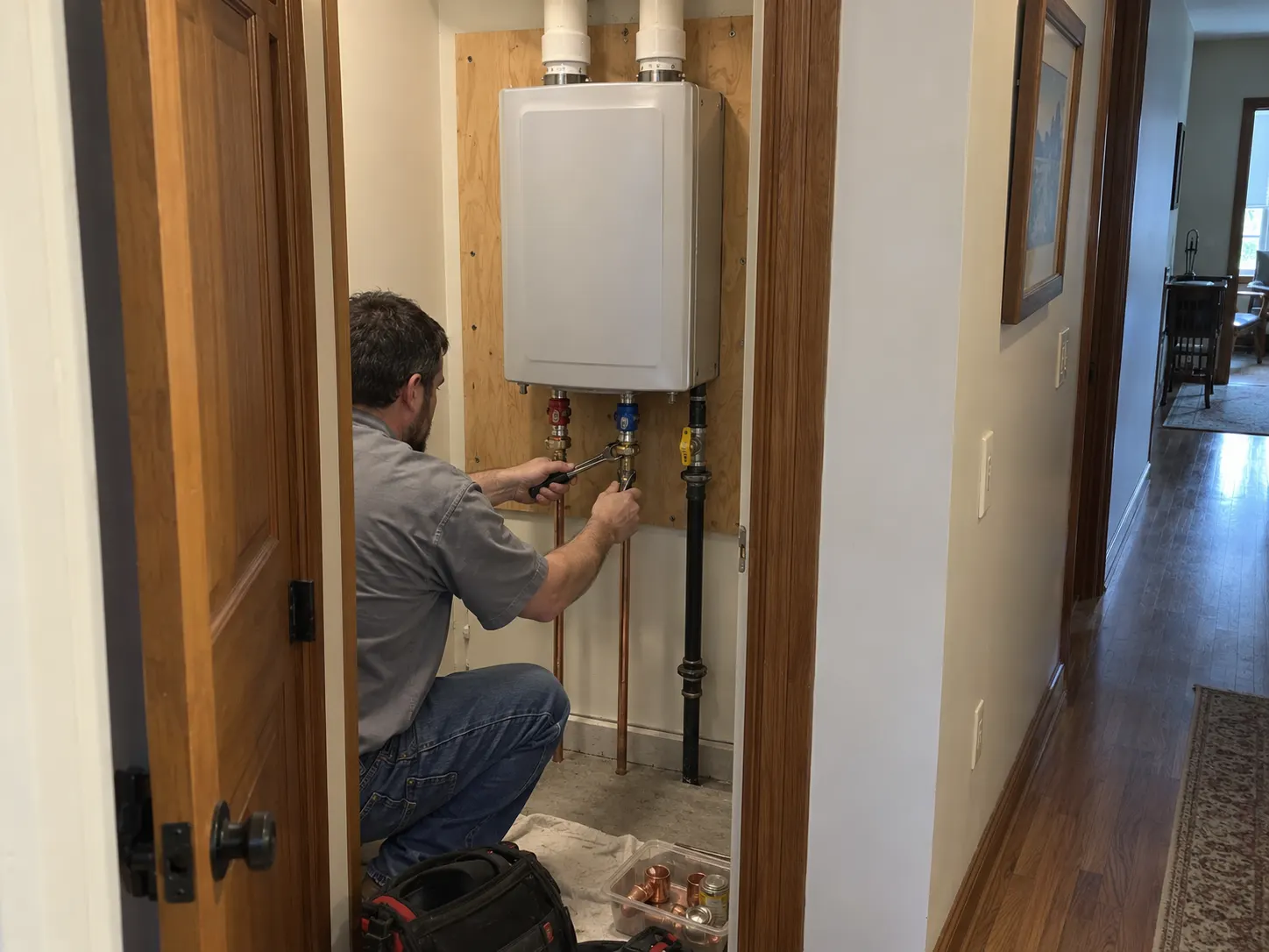An Affordable Air technician tightening the water line connections on a newly installed tankless water heater in a home closet