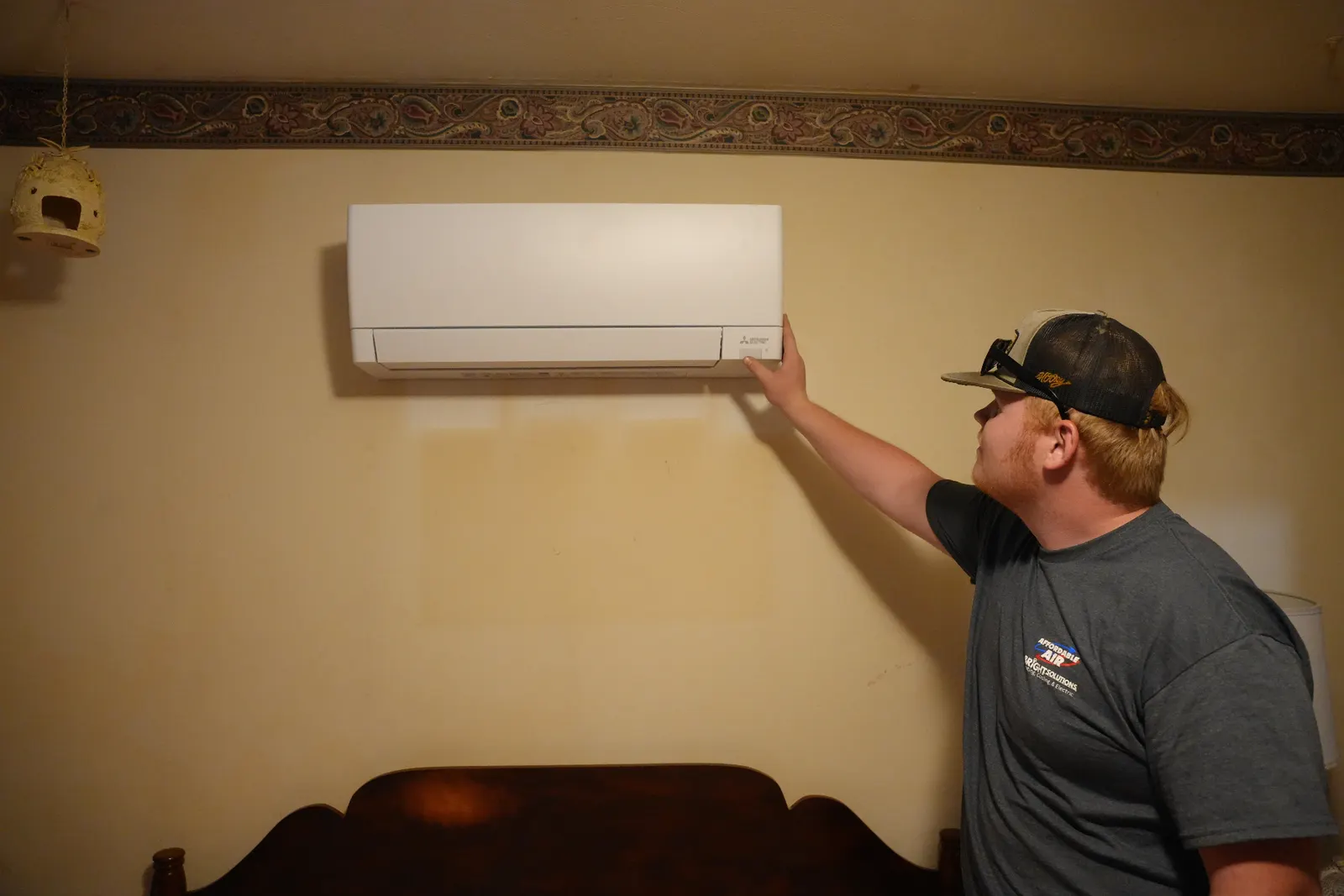 An Affordable Air technician checking a newly installed Mitsubishi Electric ductless mini-split on a bedroom wall
