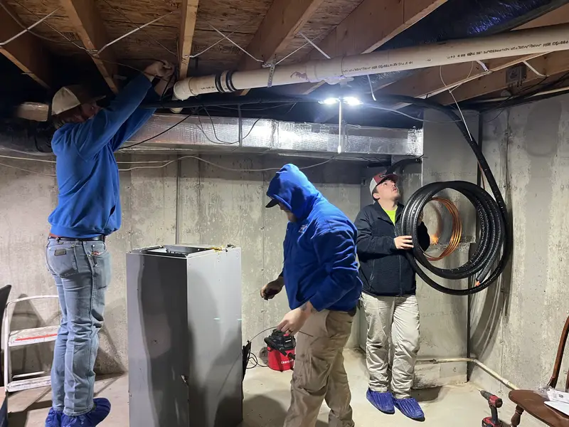 Three Affordable Air technicians routing lines and venting for a new furnace in a basement