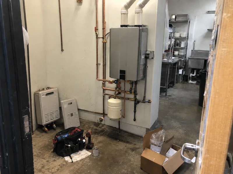 A new wall-mounted tankless water heater installed at a local business, with the old failed unit set aside on the floor