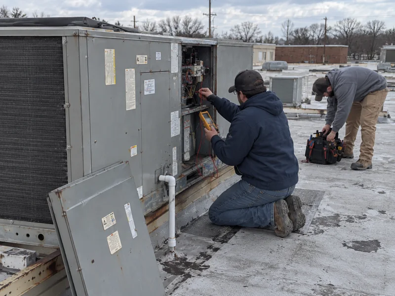 Two Affordable Air technicians testing a commercial rooftop unit's controls with a meter